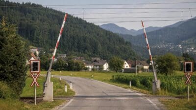 Zwei hochgeklappte Bahnschranken an einem Bahnübergang in ländlicher Umgebung.