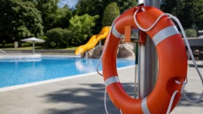 Orangefarbener Rettungsring mit silbernen Streifen hängt an einem Metallpfosten am Schwimmbecken