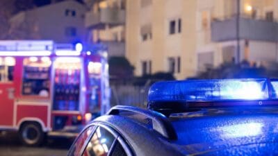 Blaues Blaulicht auf einem Polizeifahrzeug im Vordergrund mit Feuerwehrfahrzeug bei Nacht