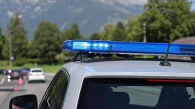 Heckansicht eines weißen Polizeiautos mit leuchtendem blauen Lichtbalken vor Bergen