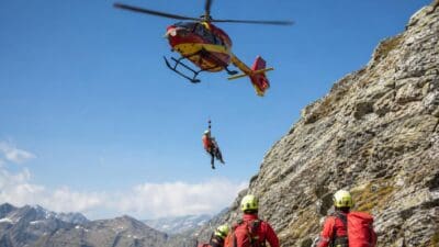 Rettungshubschrauber schwebt über steilem Fels während Bergretter eine Person bergen