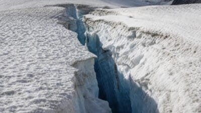 Schneebedeckte Gletscheroberfläche mit einer breiten blauen Gletscherspalte und steilen Eiswänden