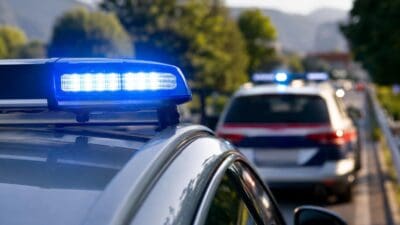Nahaufnahme eines Polizeifahrzeugs mit leuchtendem Blaulicht und einem zweiten Einsatzfahrzeug im Hintergrund
