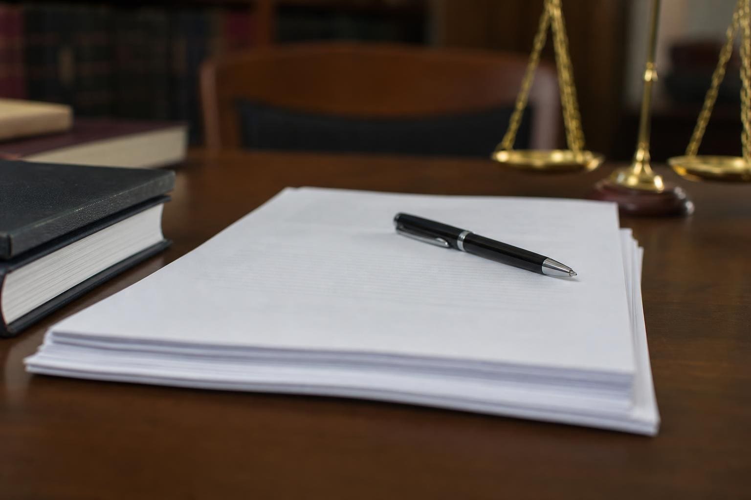 Stapel weißer Papiere mit einem Stift auf einem Holztisch neben Büchern und einer Waage
