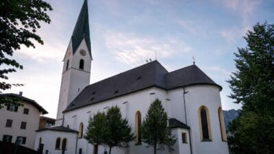 Die weiße Pfarrkirche Brixlegg mit hohem grünem Turm unter blauem Himmel