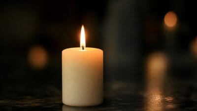 Eine brennende weiße Kerze auf einer dunklen reflektierenden Oberfläche