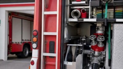 Geöffnetes Gerätefach eines roten Feuerwehrfahrzeugs mit Schläuchen Ventilen und Ausrüstung