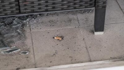 Ausgedrückter Zigarettenstummel auf gefliestem Balkonboden neben Glasscherben und Asche