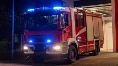 Rotes Feuerwehrfahrzeug mit blauen Blaulichtern steht nachts vor einer Halle