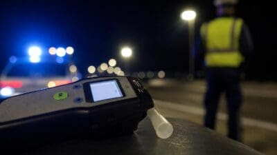 Ein Alkoholtestgerät mit Mundstück liegt im Vordergrund vor einem Polizisten bei Nacht