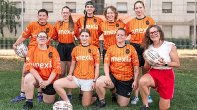 Die Mitglieder des Damenteams Anexia Tigers in orangefarbenen Trikots knien und stehen auf dem Rasen.