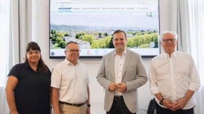 Eine Frau und drei Männer stehen vor einem großen Bildschirm mit der Website von Klagenfurt Wohnen.