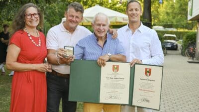 Eine Frau in rotem Kleid steht neben drei Männern, die Medaille und Urkunde präsentieren.