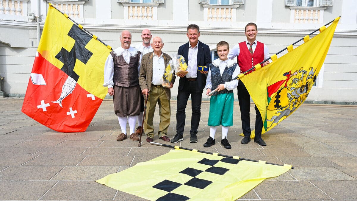 Gruppe von Männern und einem Jungen mit großen Fahnen auf einem Steinplatz vor einem Gebäude