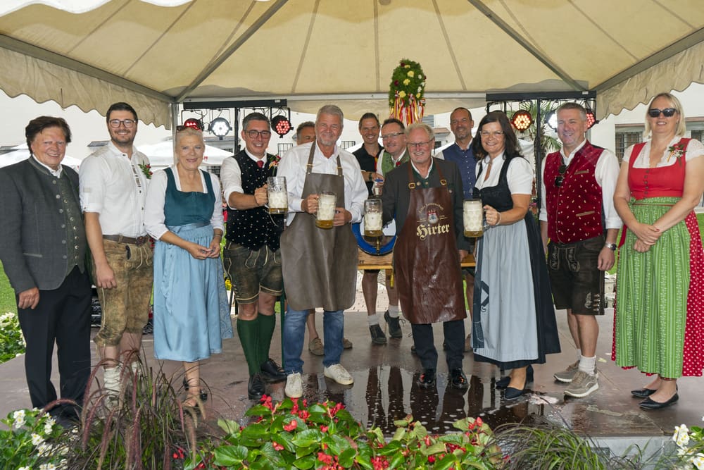 Mehrere Personen in traditioneller Tracht halten Bierkrüge unter einem weißen Zelt.