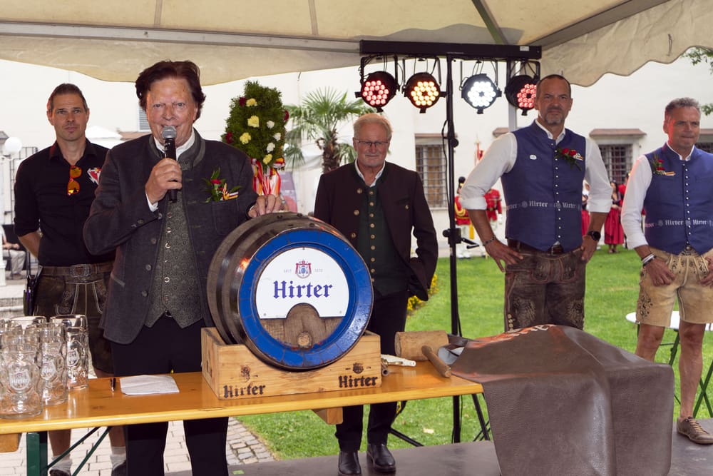 Ein Mann in Tracht spricht in ein Mikrofon neben einem Bierfass auf einer Bühne