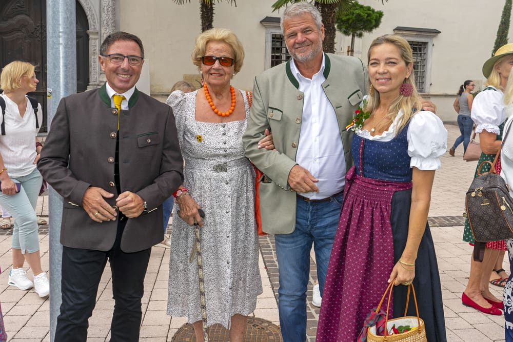 Vier Erwachsene in traditioneller Tracht stehen lächelnd beieinander vor einem Gebäude.