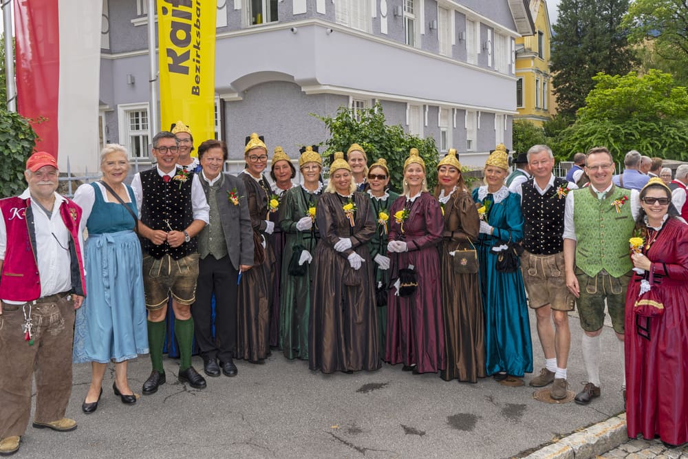Gruppe von Frauen und Männern in traditionellen Trachten mit goldenen Hüten vor einem Gebäude.
