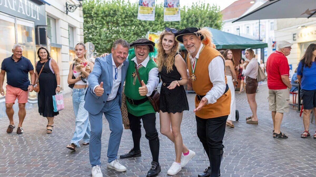 Gruppe von Menschen in bunter und traditioneller Kleidung posiert fröhlich auf einer gepflasterten Altstadtstraße.
