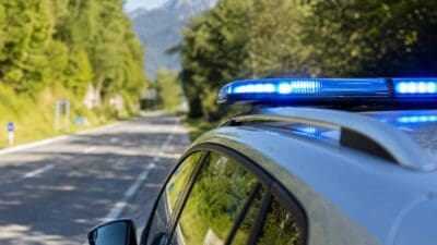 Polizeifahrzeug mit aktiviertem Blaulicht auf einer Landstraße in bergiger Landschaft