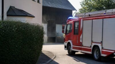 Rotes Feuerwehrauto steht vor einem Haus mit Rauch aus dem Keller