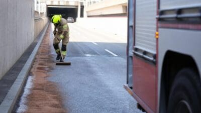 Feuerwehrmann in gelbem Helm und Schutzkleidung reinigt mit einem Werkzeug die nasse Fahrbahn in einer Unterführung