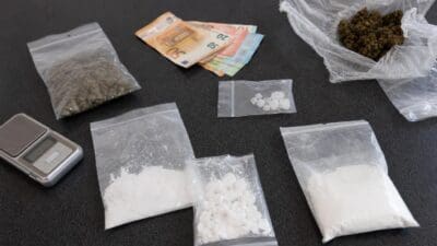Mehrere Plastikbeutel mit Cannabis, Kokain und Bargeld liegen neben einer digitalen Waage auf einem Tisch.