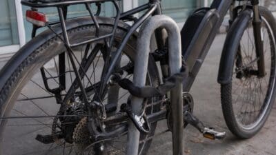 Nahaufnahme eines schwarzen E-Bikes, das mit einem Bügelschloss und einer Kette an einem Metallpfosten gesichert ist.