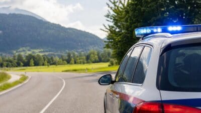 Heckansicht eines Polizeifahrzeugs mit aktiviertem Blaulicht auf einer kurvigen Landstraße in den Bergen