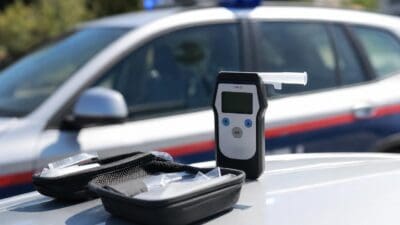 Alkoholtester mit Mundstück steht auf der Motorhaube eines Polizeiautos neben offener Tasche mit Einwegmundstücken