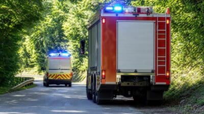 Rotes Feuerwehrfahrzeug und gelber Rettungswagen mit Blaulicht auf einer Waldstraße