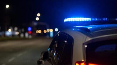 Heck eines weißen Einsatzfahrzeugs mit blauem Blaulichtbalken und roten Rücklichtern bei Nacht auf einer Straße