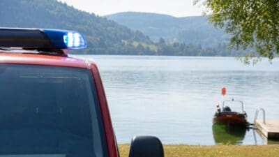 Rotes Einsatzfahrzeug mit blauem Blaulicht am Ufer des Längsees und Boot am Steg