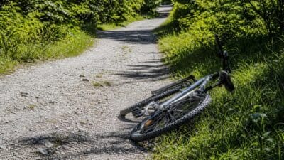 Ein umgestürztes Fahrrad liegt auf einem Kiesweg im Wald.