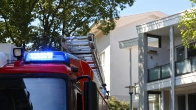 Rotes Feuerwehrfahrzeug mit blauem Blaulicht vor einem weißen Wohngebäude