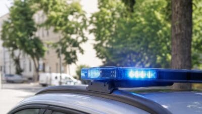 Nahaufnahme eines aktivierten blauen Blaulichts auf dem Dach eines grauen Polizeifahrzeugs.