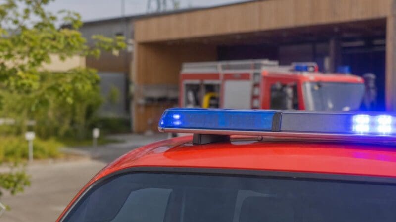 Blaues Blaulicht leuchtet auf dem Dach eines roten Feuerwehrfahrzeugs vor einer Halle.