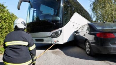 Ein Feuerwehrmann in Uniform sichert mit einem Seil einen weißen Reisebus neben einem Pkw