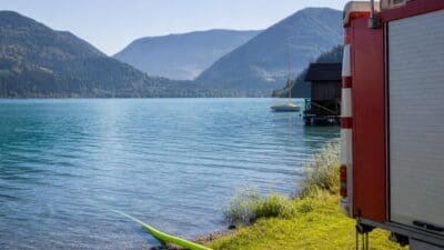 Rotes Feuerwehrfahrzeug mit grünem Schlauch am Ufer des Weißensees vor Berglandschaft