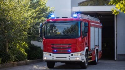 Rotes Feuerwehrfahrzeug mit aktiviertem Blaulicht steht vor einer geöffneten Feuerwehrgarage.