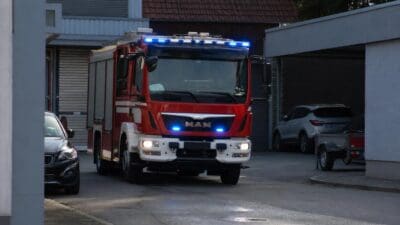 Frontansicht eines roten Feuerwehrfahrzeugs mit blauem Blaulicht vor Gebäuden