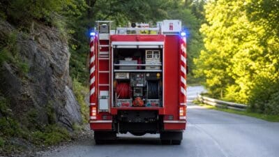 Rotes Feuerwehrauto mit geöffnetem Heck und Blaulicht auf einer Straße neben einem Felsen