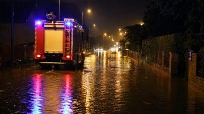 Rotes Feuerwehrfahrzeug mit Blaulicht auf überfluteter Straße bei Nacht