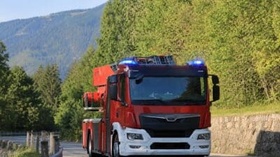 Rotes Feuerwehrfahrzeug mit blau leuchtendem Blaulicht auf einer Straße in bergiger Landschaft