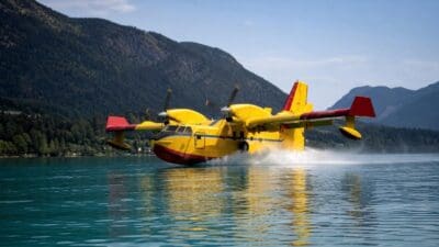 Gelbes Löschflugzeug auf dem türkisfarbenen Wasser des Weißensees mit Bergen im Hintergrund