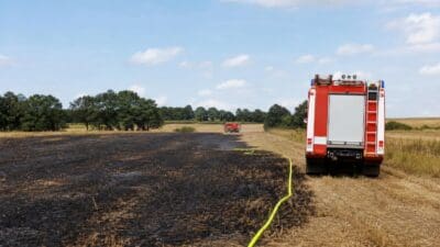 Rotes Feuerwehrauto auf einem schwarz verbrannten Feld mit gelbem Schlauch