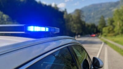 Nahaufnahme eines blauen Blaulichts auf dem Dach eines silbernen Polizeifahrzeugs an einer Straße mit Bergen im Hintergrund