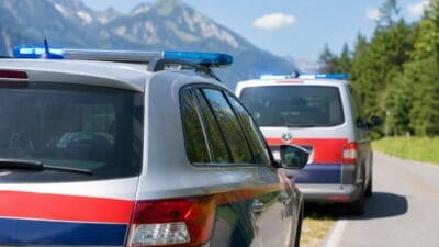 Zwei Polizeifahrzeuge mit Blaulicht auf einer Straße vor Bergen