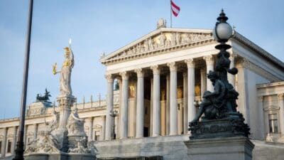 Das österreichische Parlamentsgebäude in Wien mit wehender Fahne und Statuen davor.