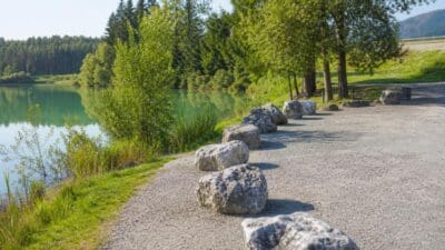 Kiesweg am Ufer des Tristacher Sees mit großen Steinen als Begrenzung